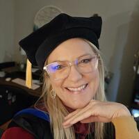 light skinned woman with glasses in commencement regalia